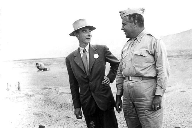 Two men stand next to a mangled piece of metal equipment in the desert.