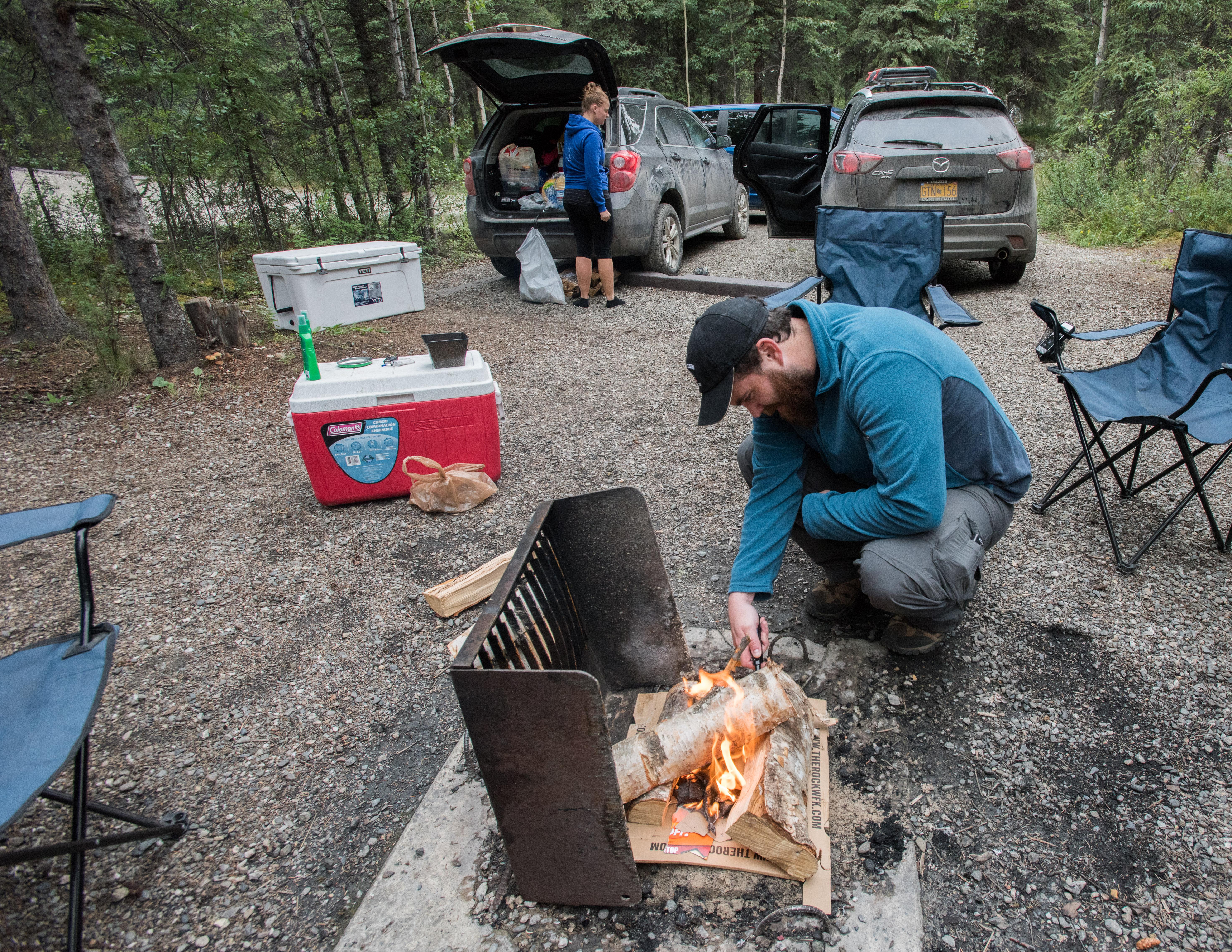 a man lighting a campfire, and a woman pulling gear out of a car