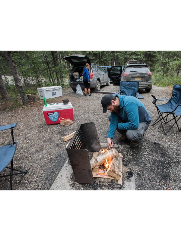 a man lighting a campfire, and a woman pulling gear out of a car