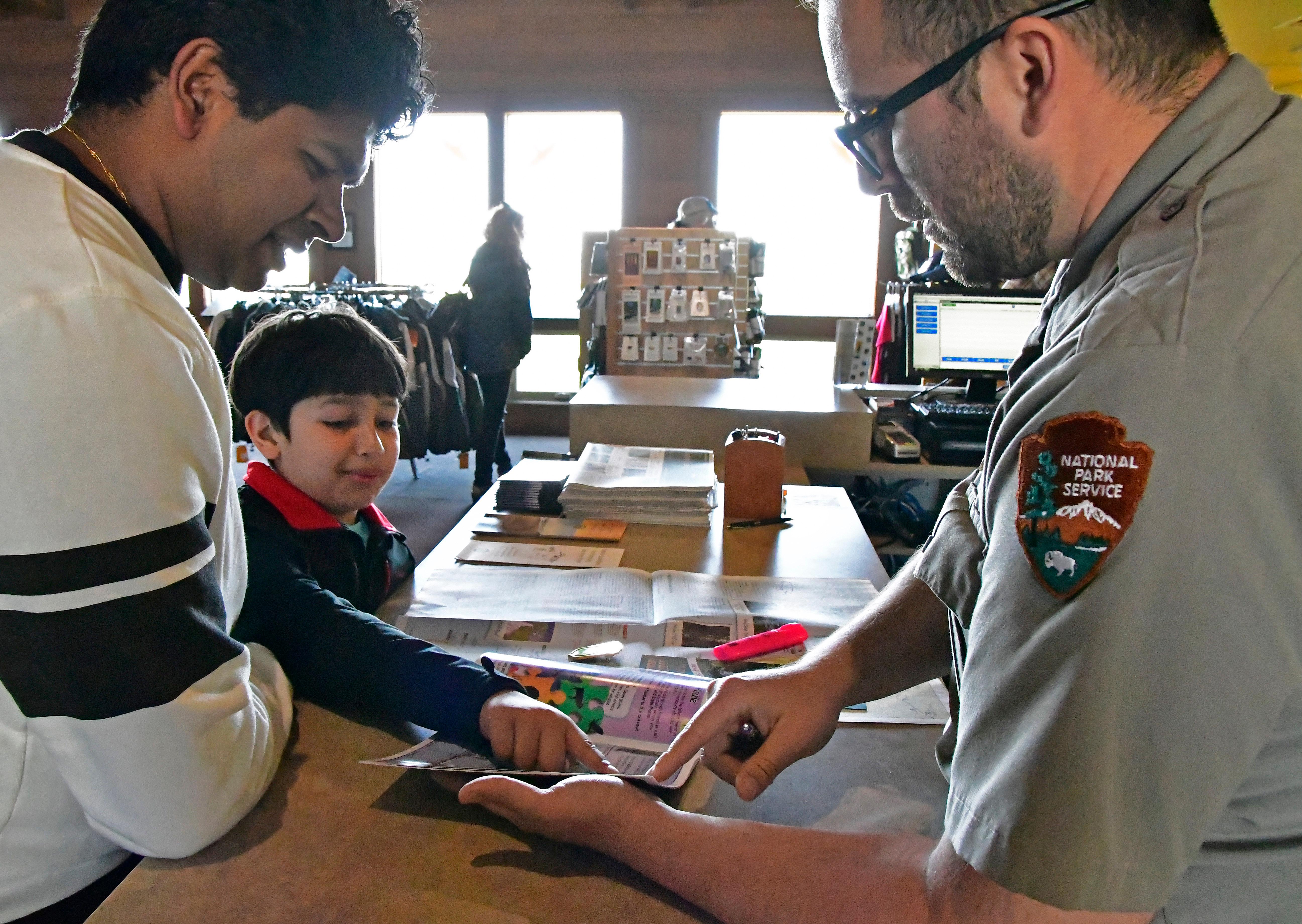 A father, young son and a park ranger look over a book