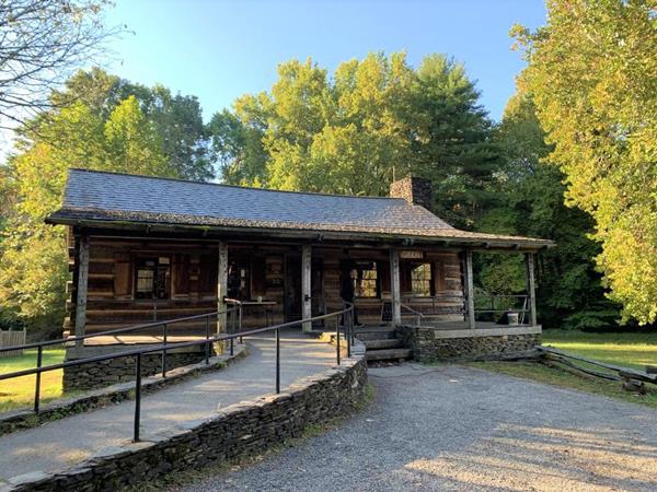 A park visitor center built like a log cabin with a covered porch, chimney, and paved approach ramp.