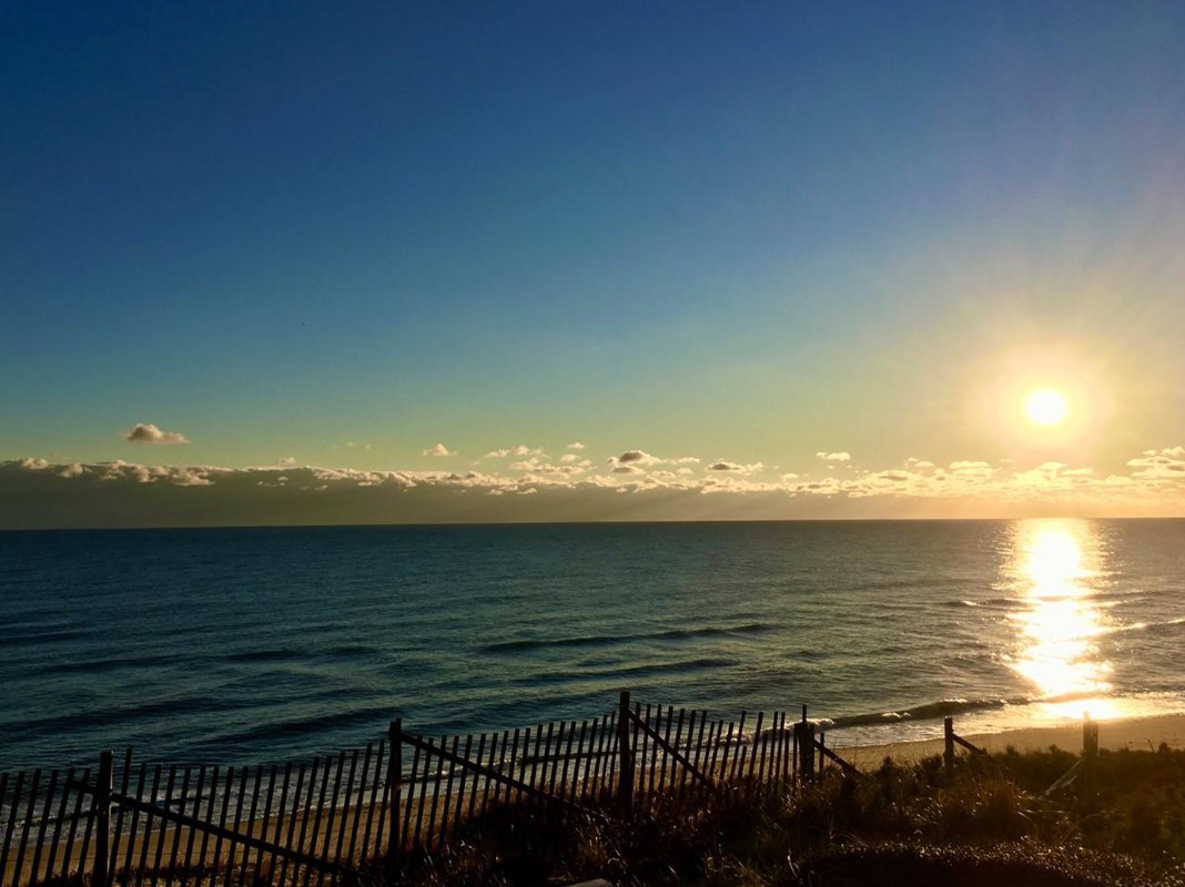 A brilliant sun rises over the ocean reflecting light on the water's surface.