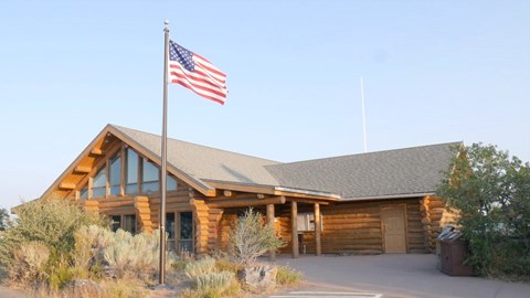 Log-built South Rim Visitor Center with an American flag, sagebrush in the foreground