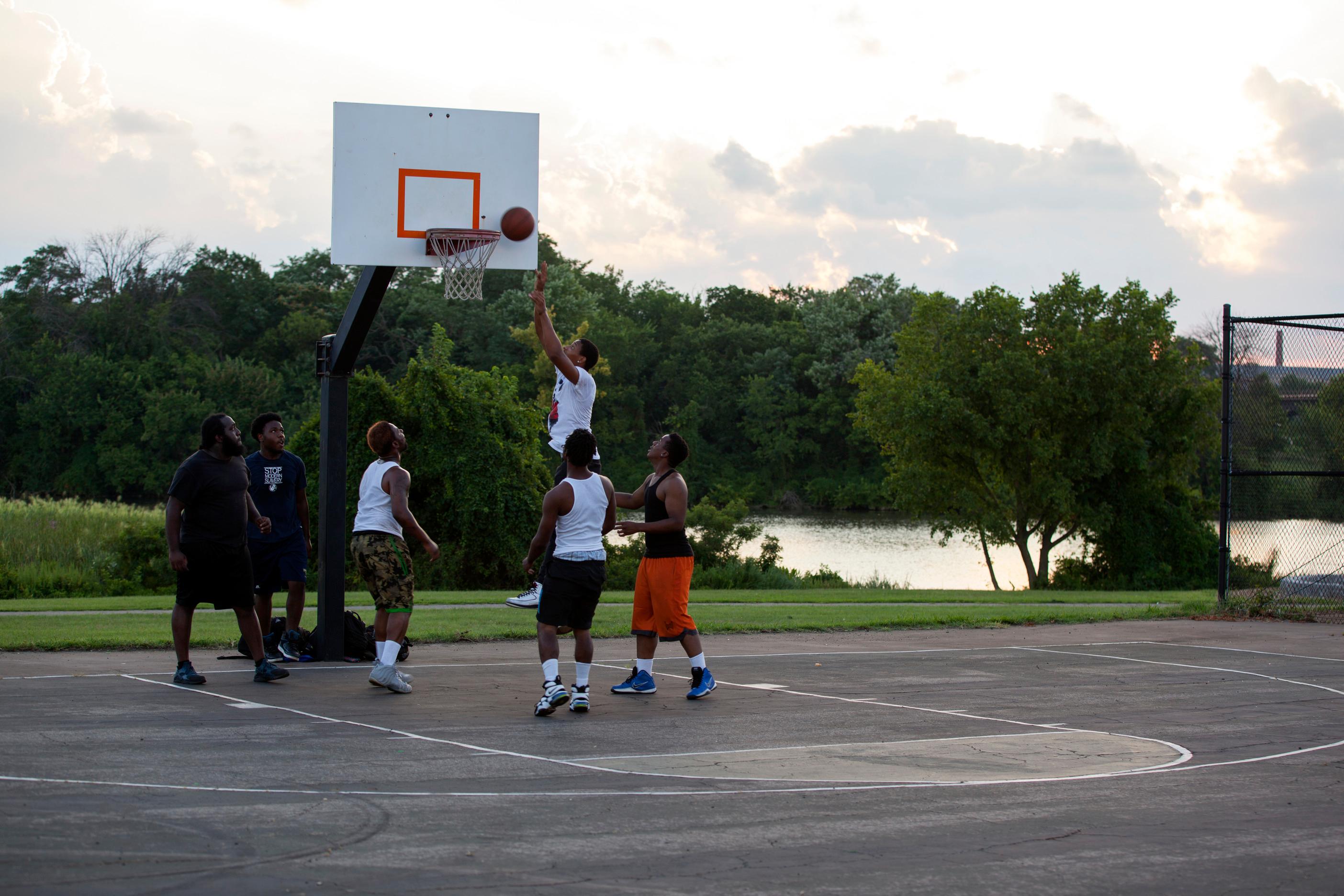 A few men are playing basketball at Anacostia with the Anacostia River in the background.
