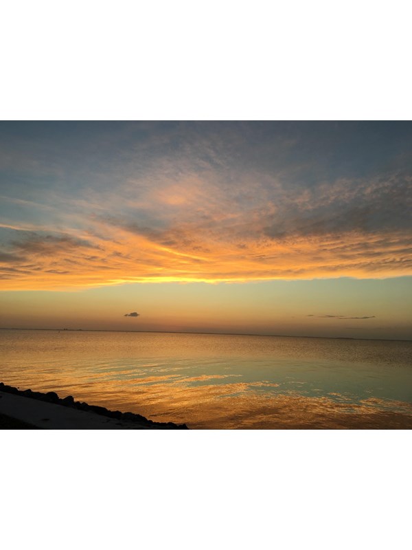 Golden orange sunset mirrored in the calm waters of the bay