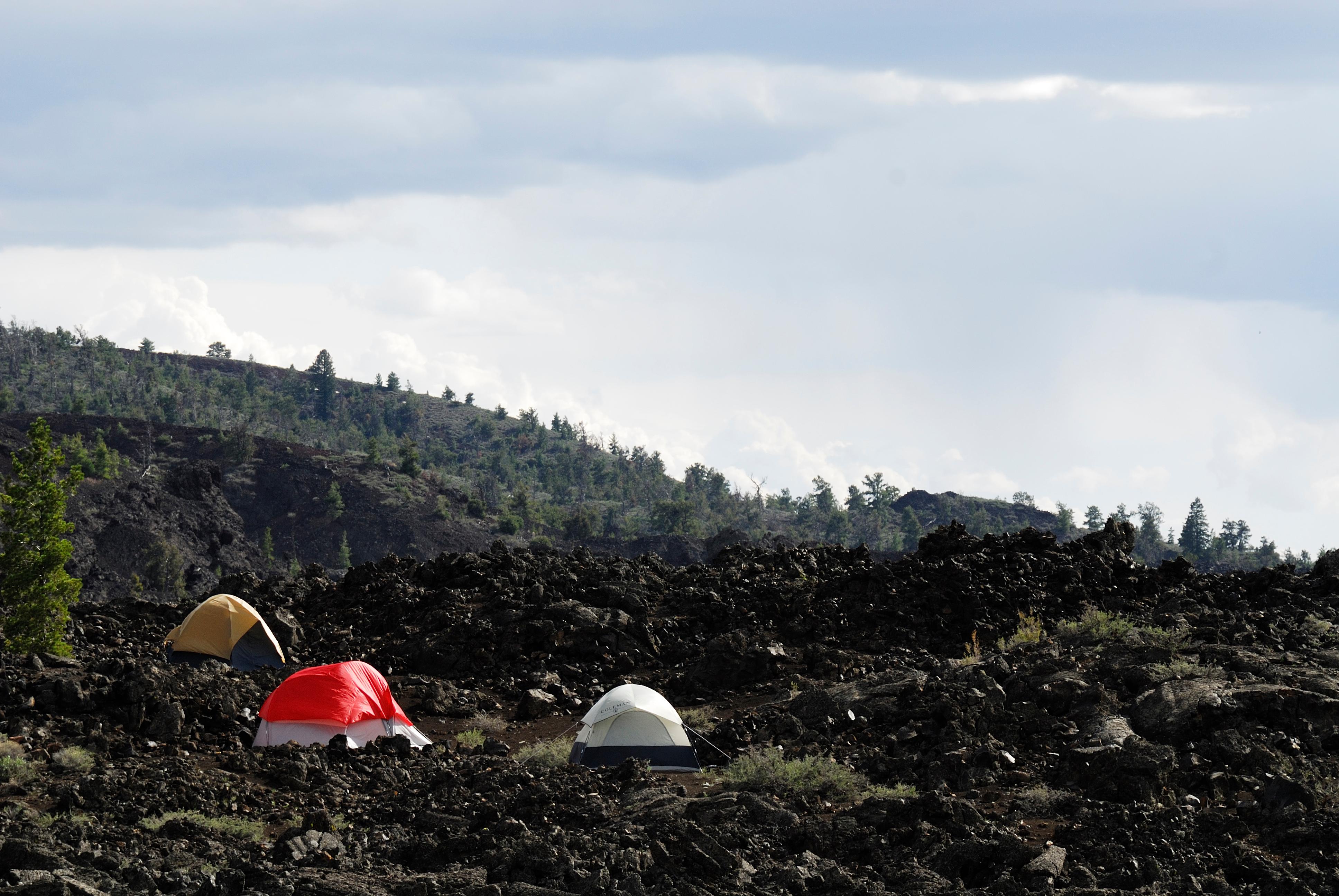 three tents on a hill of black lava rocks with a dark hill covered with trees in the distance
