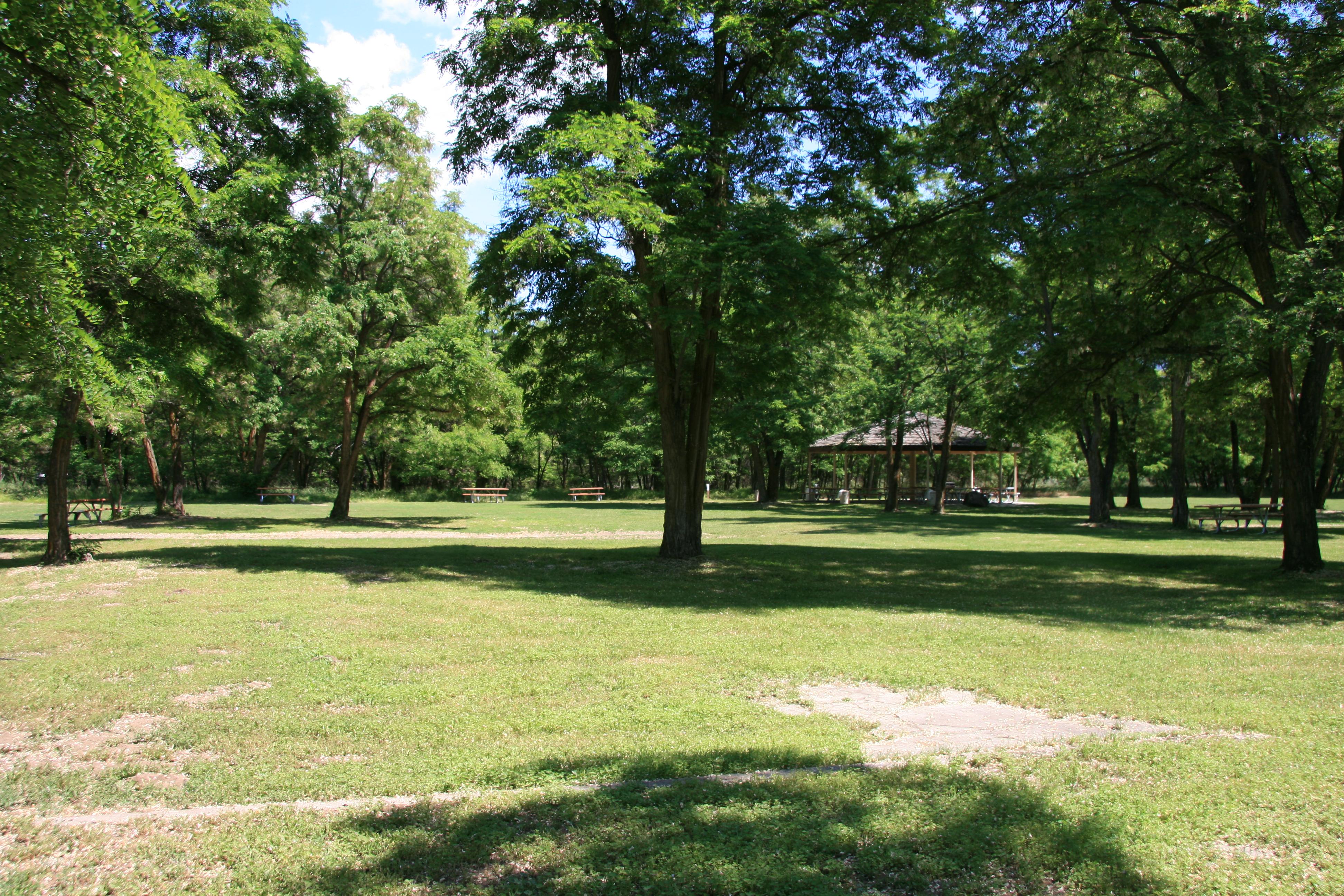 A grassy area with picnic tables and a gazebo beyond.