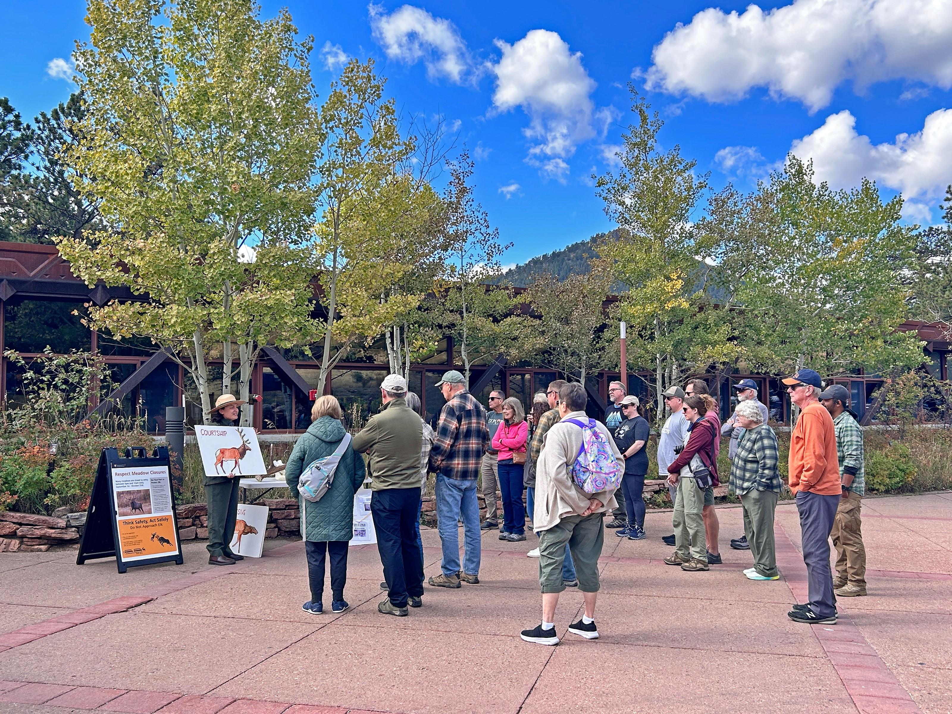 A park ranger is standing outside of the Beaver Meadows Visitor Center, leading a program