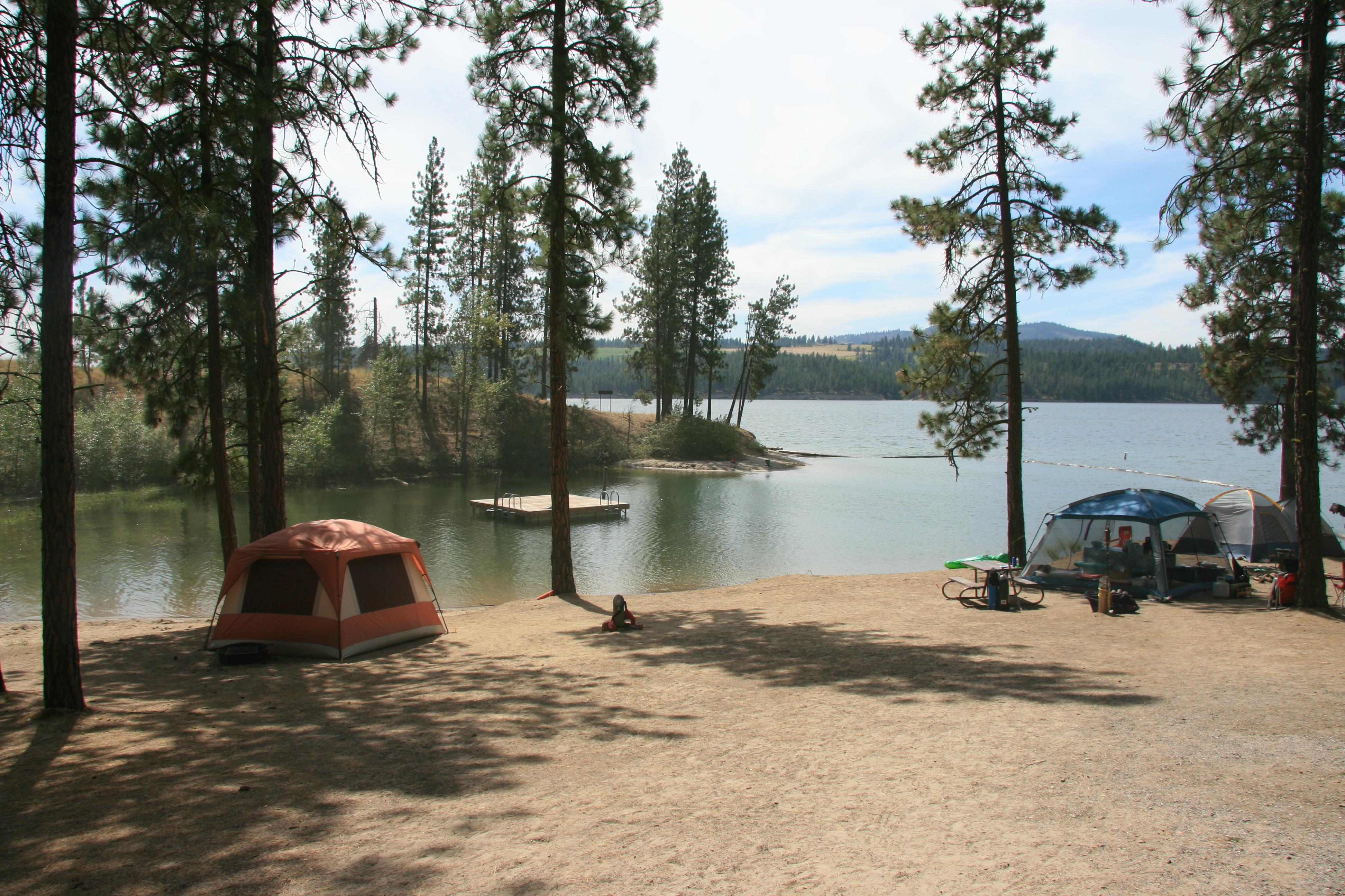 Tents are set up in campsites along the shore of the lake with a swim dock just beyond.