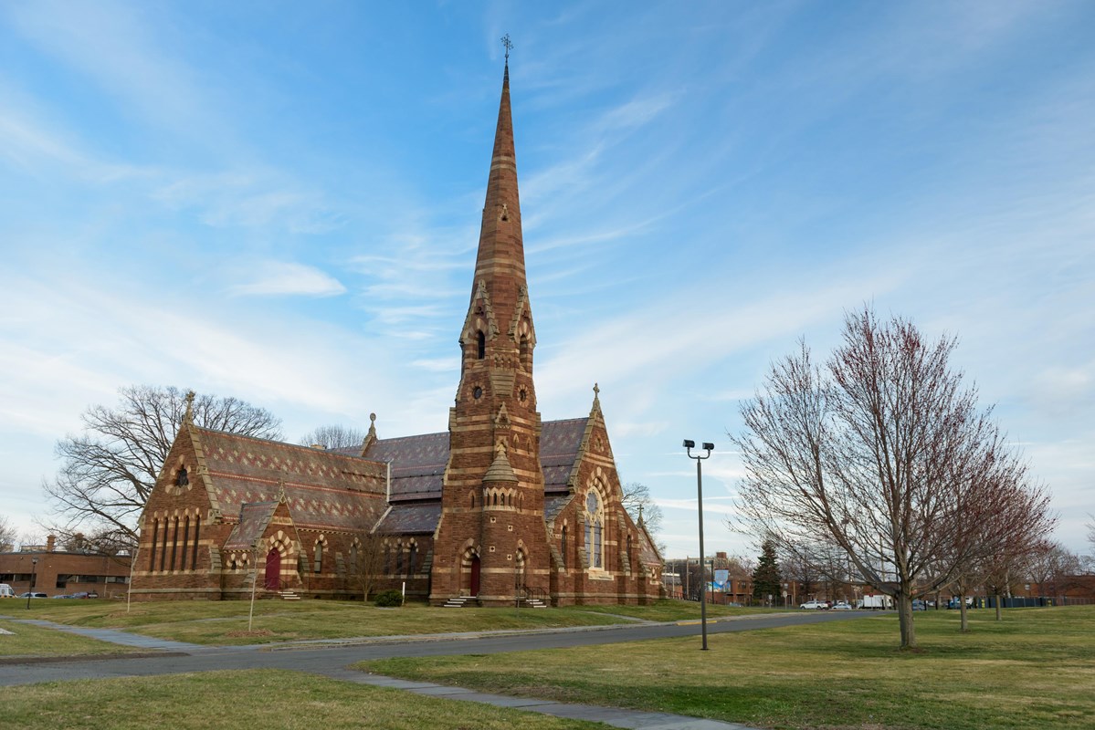 A church and trees against the backdrop of a bight blue sky and clouds. 