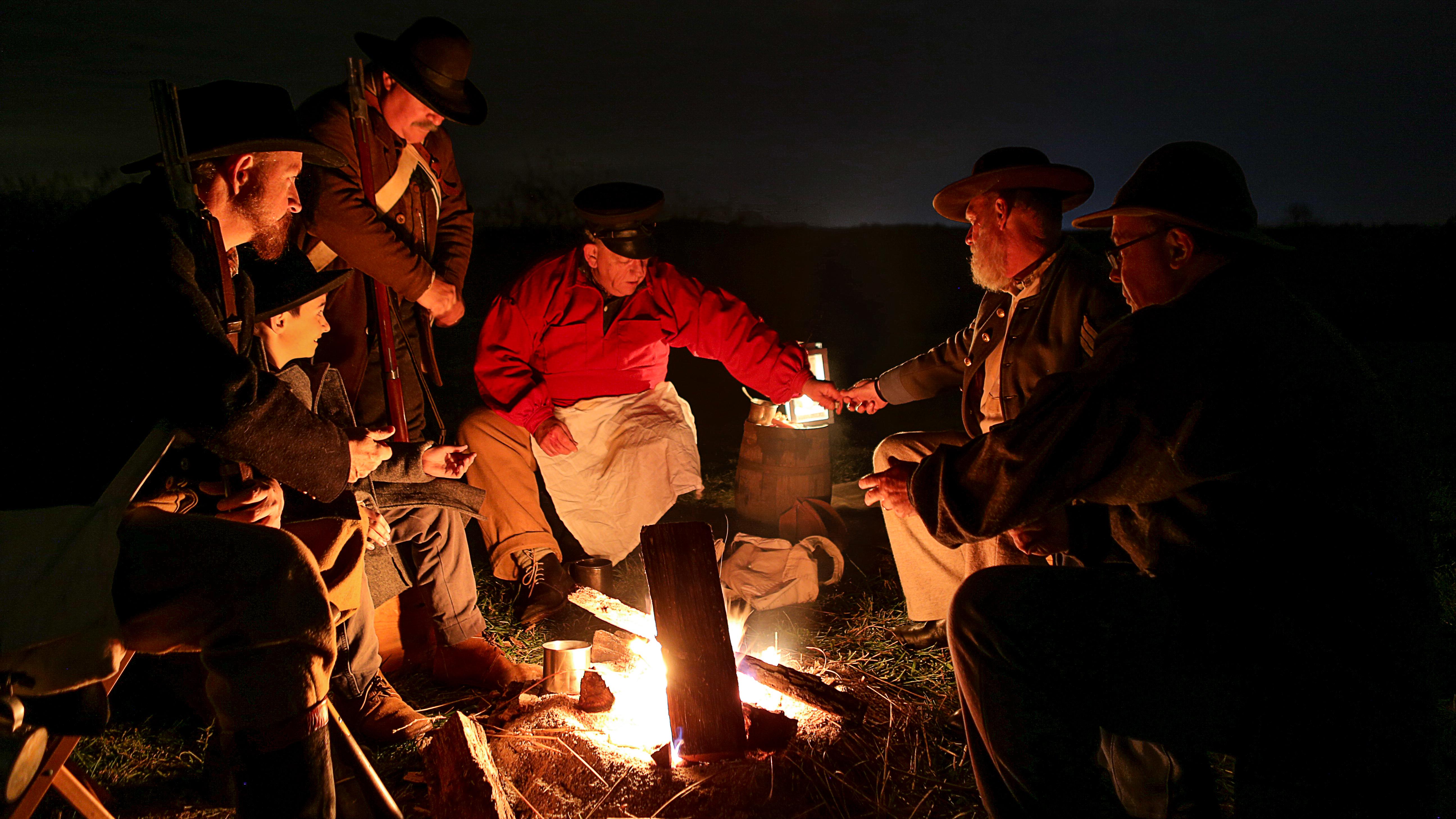 Men in reproduction uniforms talk around a campfire