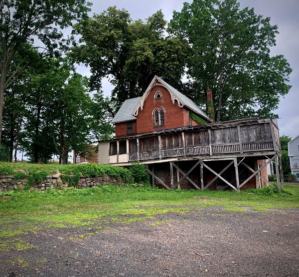 A red brown building with a wooden enclosed spaced in front of trees on a cloudy day.