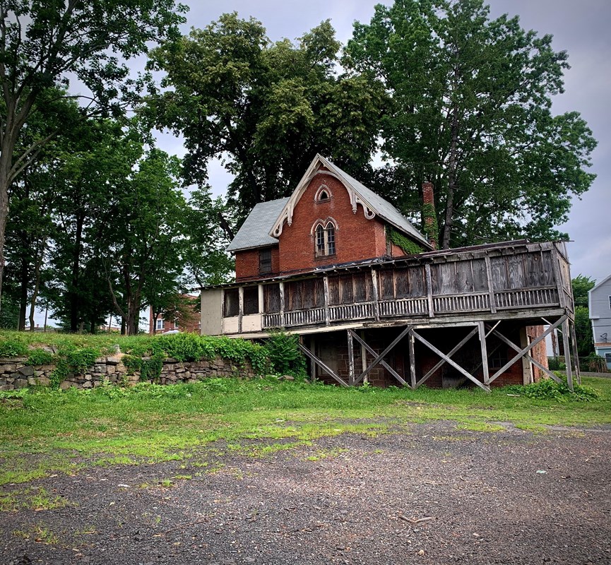 A red brown building with a wooden enclosed spaced in front of trees on a cloudy day. 