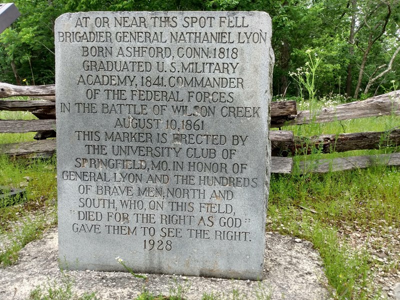 Lyon Marker A stone marker with engraving sits in front of a wooden fence and trees