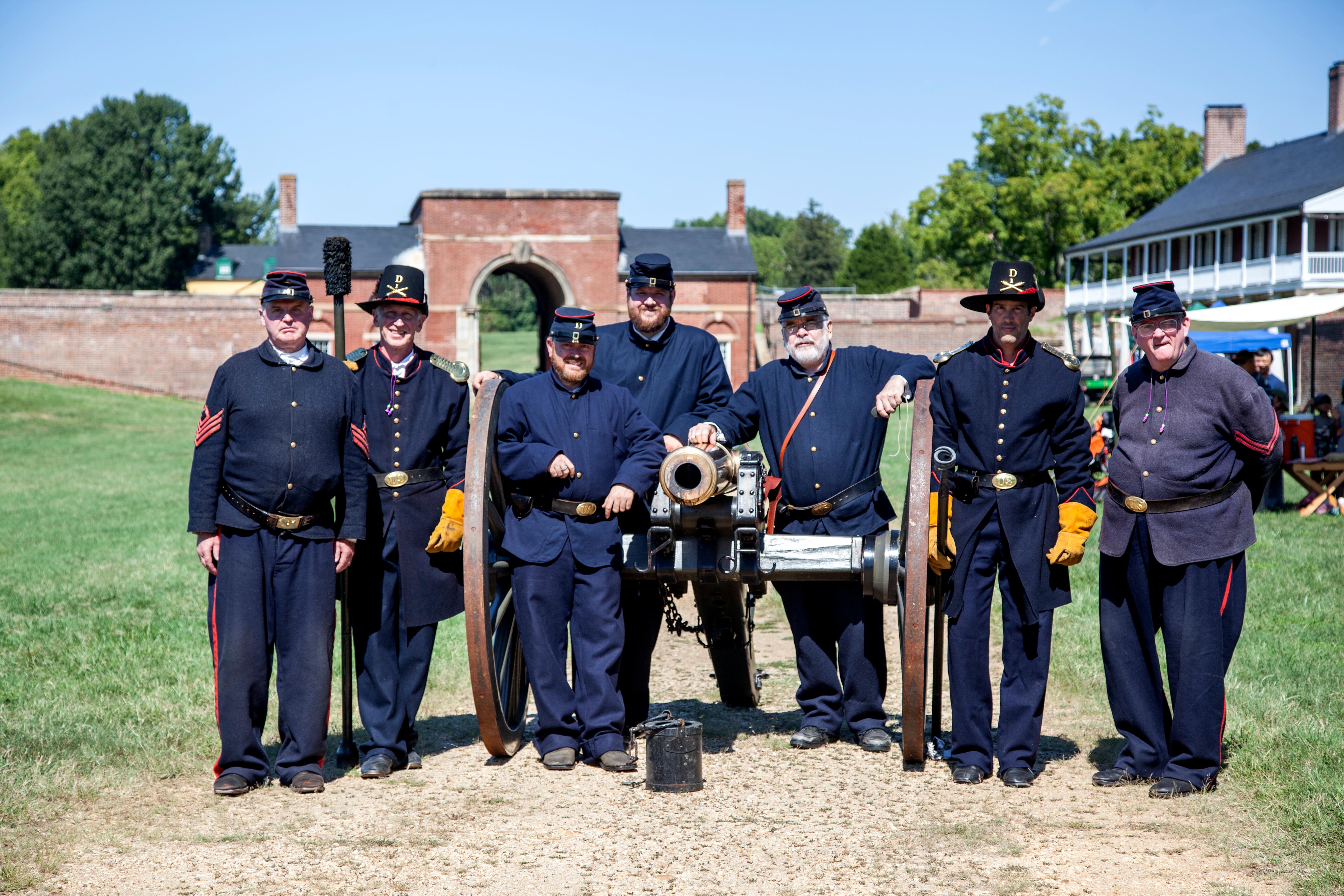 Men in blue army uniforms pose by a cannon.