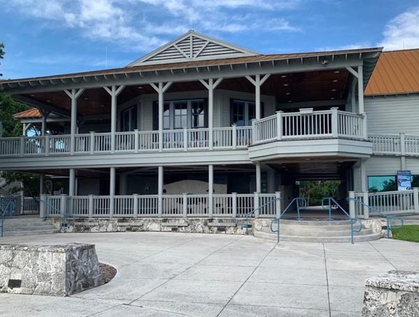 Two story grey building with peaked roof and sweeping covered porch on the second floor.
