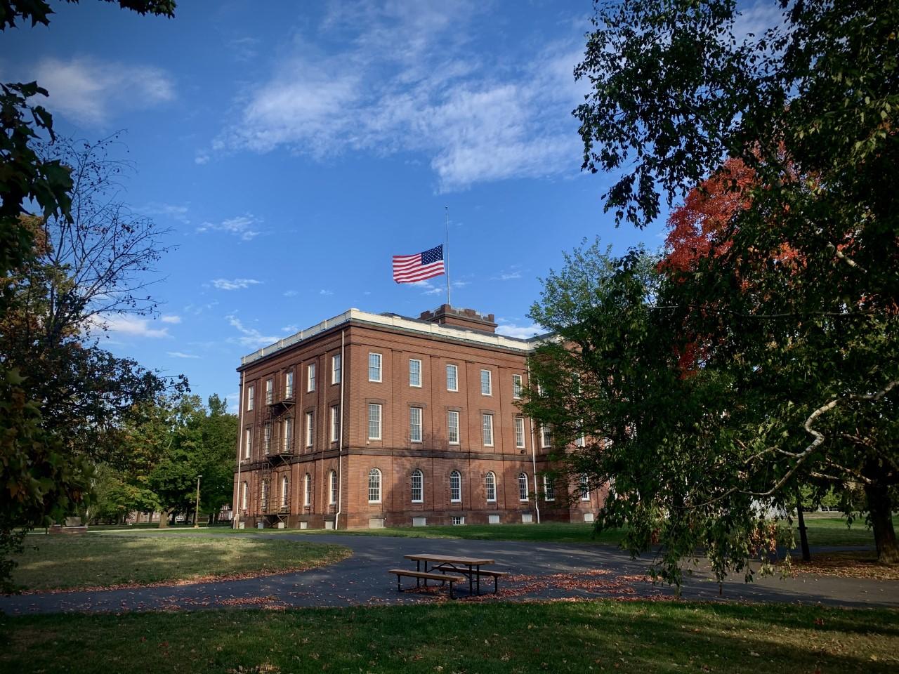 The Springfield Armory Main Arsenal on a fall day, with blue skies and the flag at half staff.