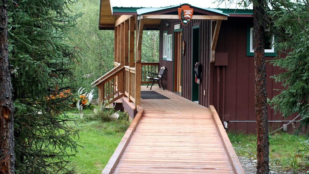 A wooden deck ramp leading to a wooden building through trees.