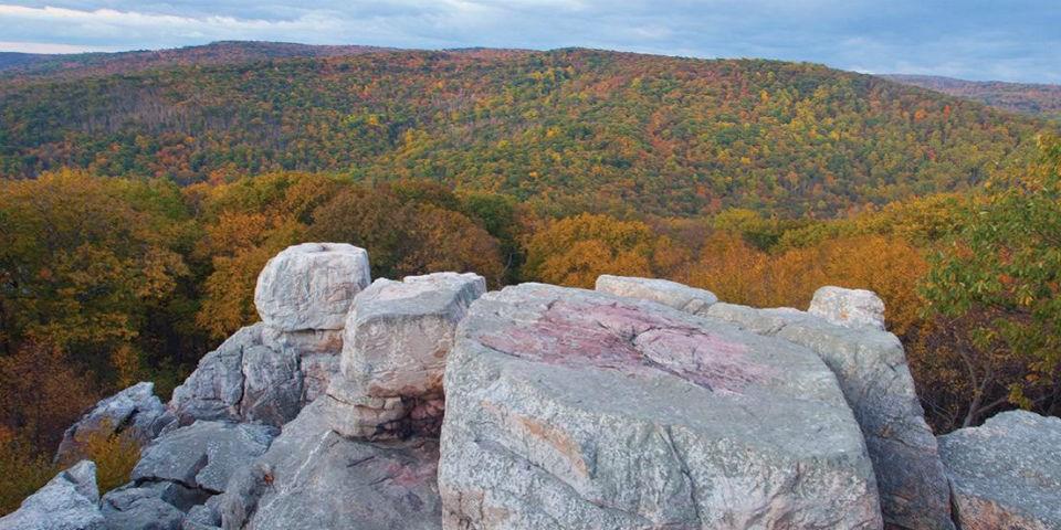 A large rocky outcropping overlooking a mountainside with fall foliage.