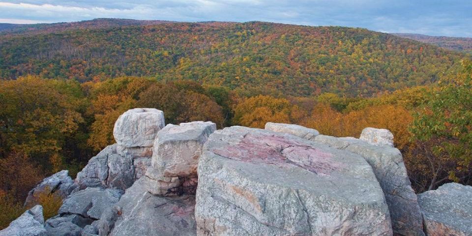 A large rocky outcropping overlooking a mountainside with fall foliage. 