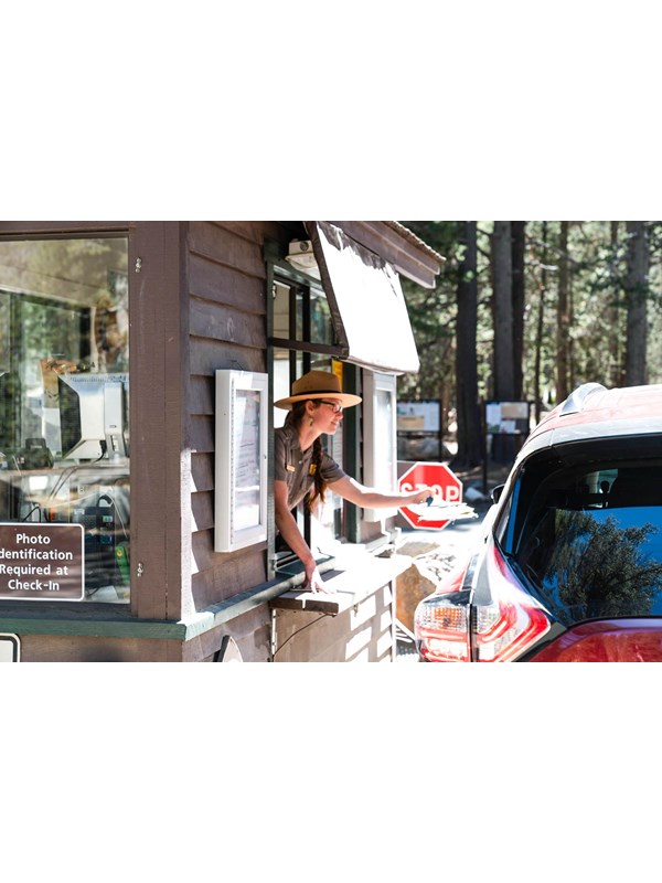 A female park ranger leans out of a kiosk window to help a visitor who is in their car.