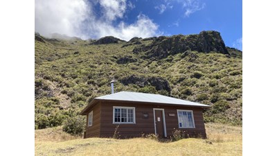 brown building at base of sloping cliff with greenery and blue sky