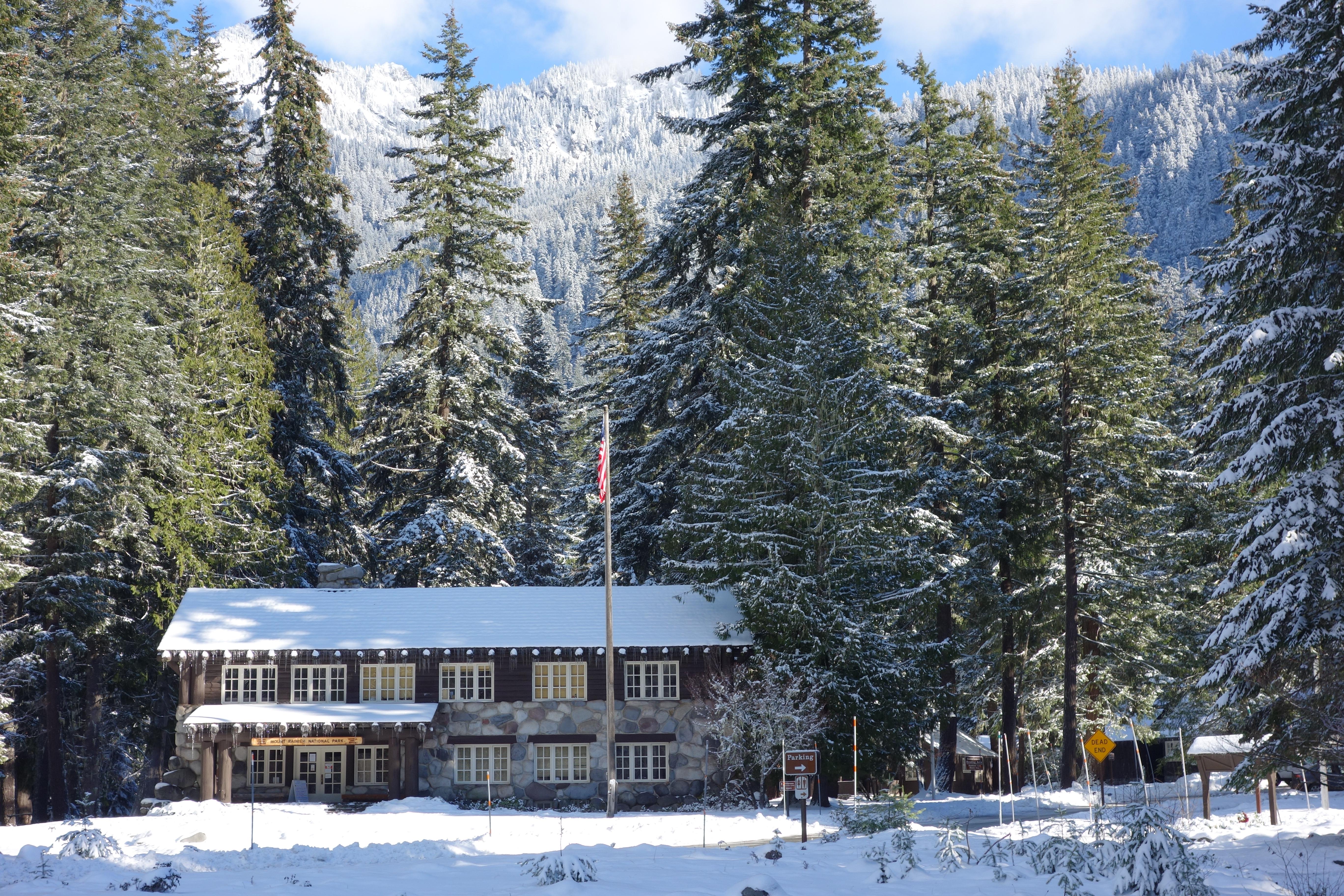 A two-story wood and stone building frosted by snow and surrounded by tall trees.