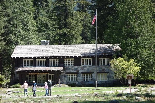 Four visitors walk up a path towards the entrance of a rustic two-story wood and stone building.