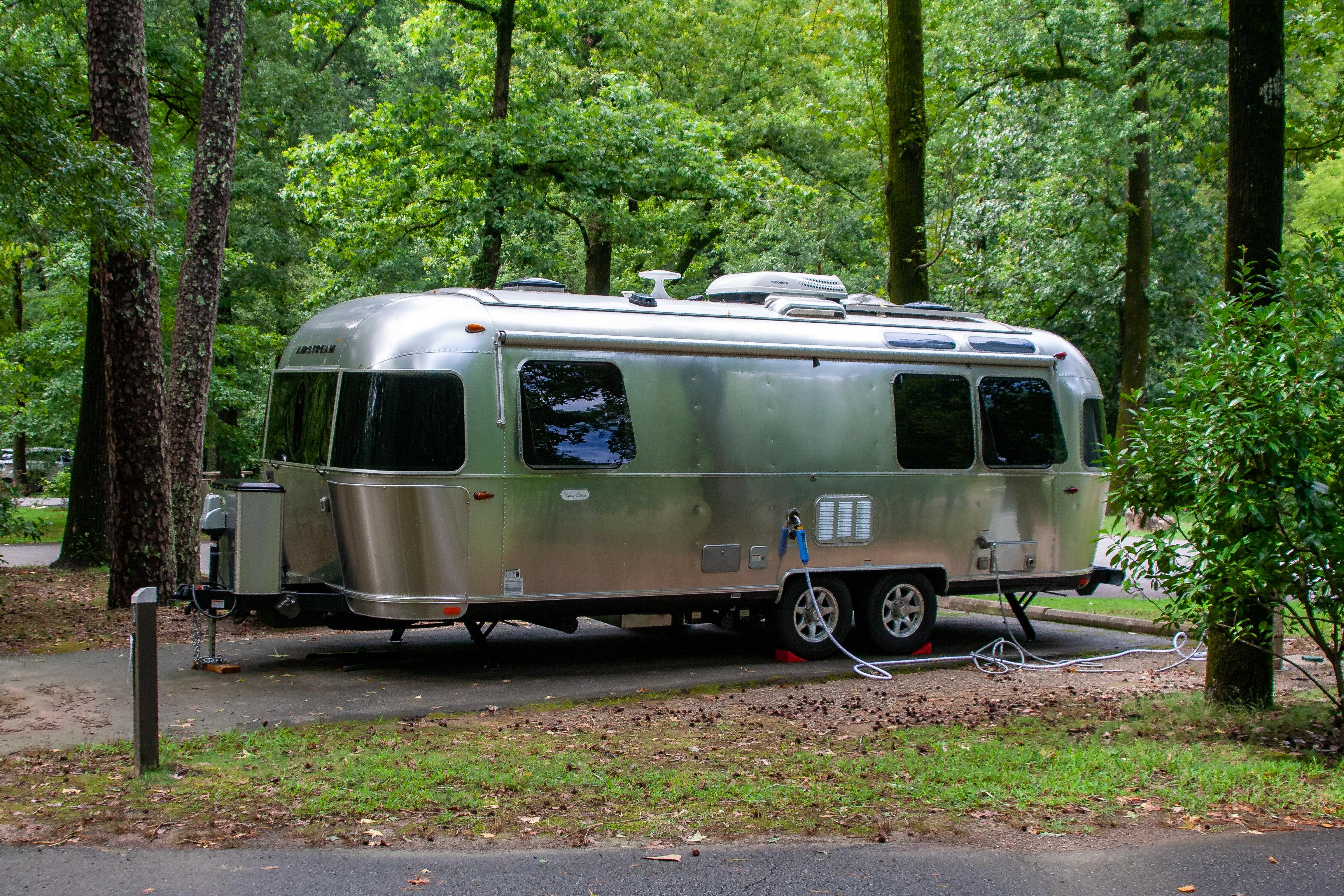 A silver RV camper parked on a lot and hooked up to power