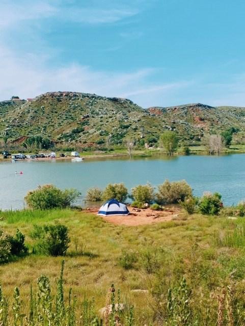 Camping in meadow by Harbor Bay.  There are mesas in the background and the lake and sky are blue.