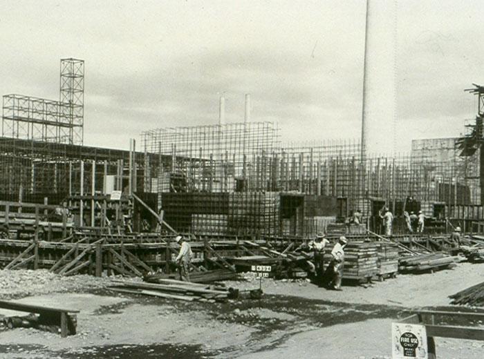 Black and white photograph of a construction site with scaffolding and workers visible.