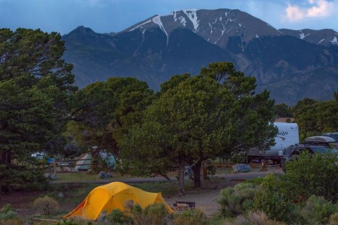 A tent and RV in a campground with small trees and a snow-capped mountain behind