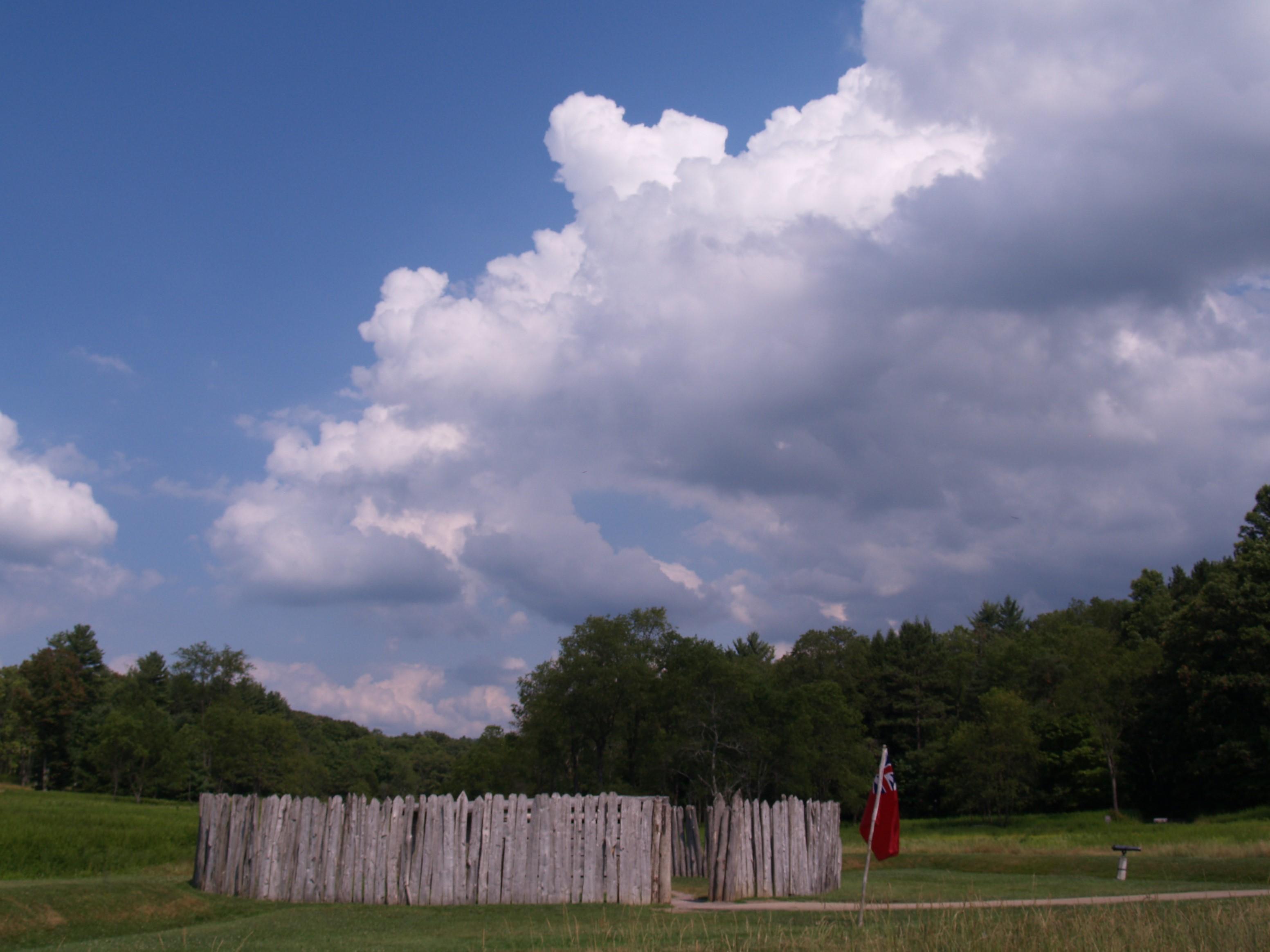 Circular stockade in the middle of a meadow. Dramatic clouds build in the blue sky.