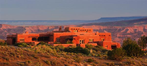 Puebloan style multi-level building against red badlands, blue mesas, and blue sky at dawn.