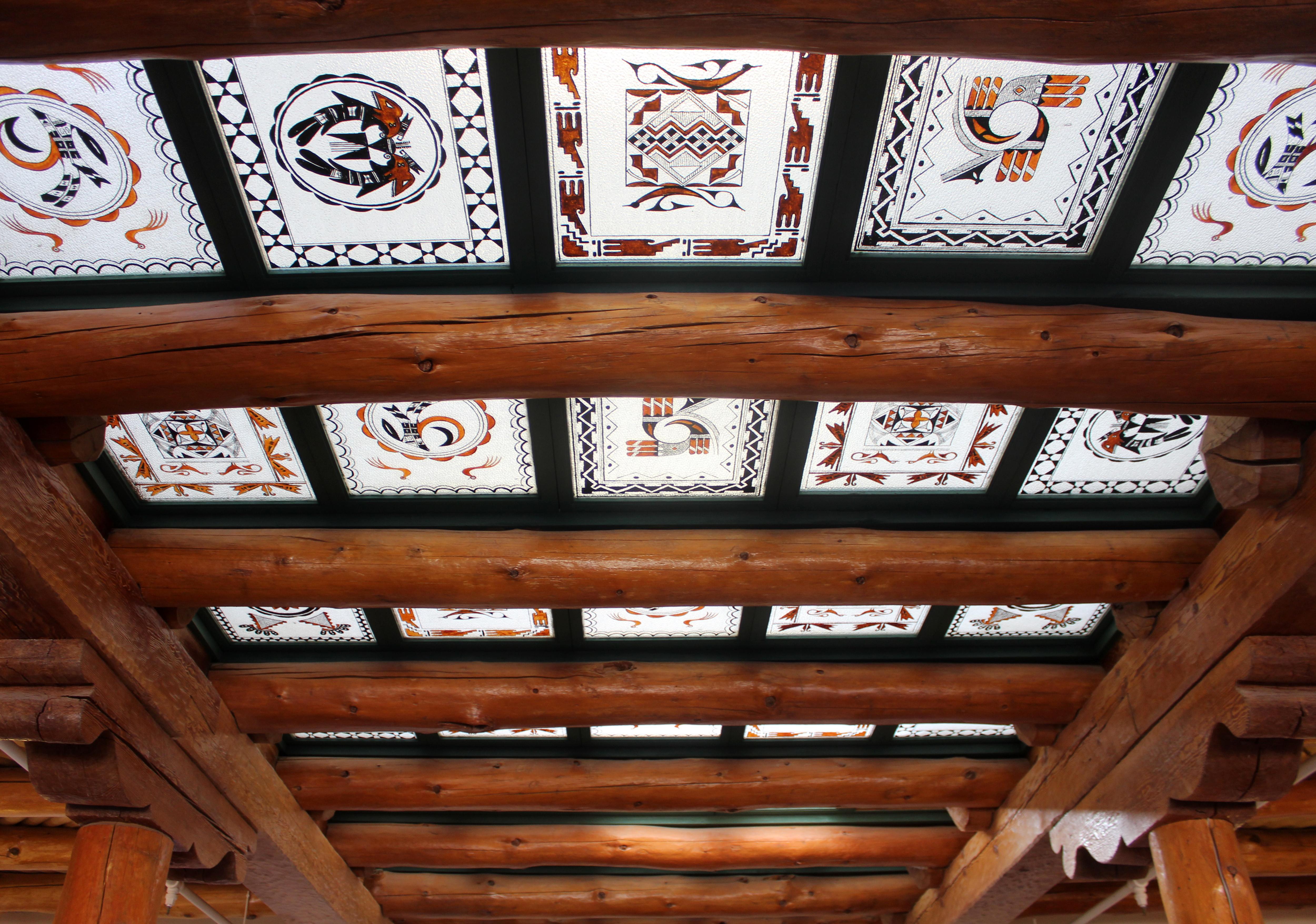 White glass painted in black and brown indigenous designs with viga and wood frames in ceiling.