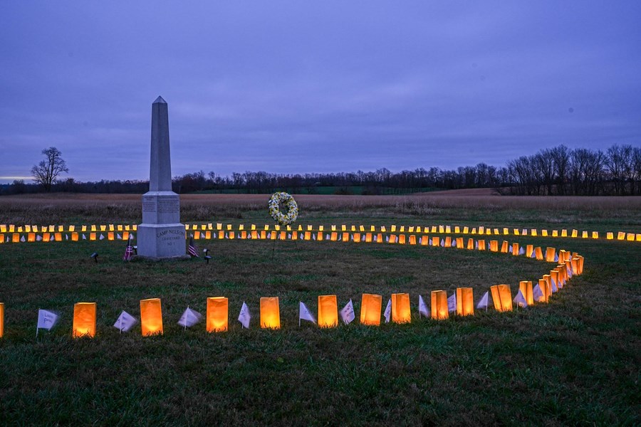 A stone obelisk in a grass field surrounded by luminary bags