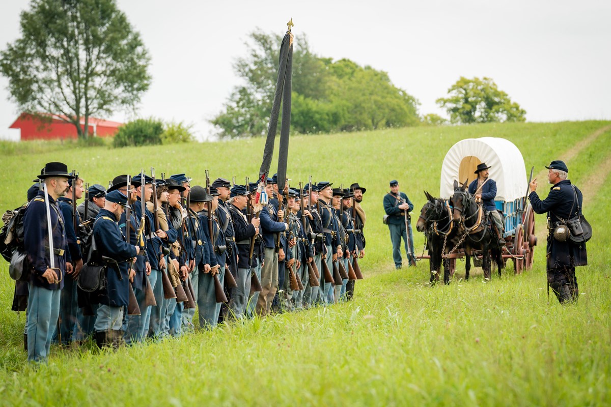 Living historians portraying US soldiers in a grass field with a wagon.