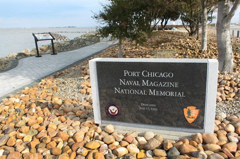 Park signs sitting in rock bed. Trees and bay in background.
