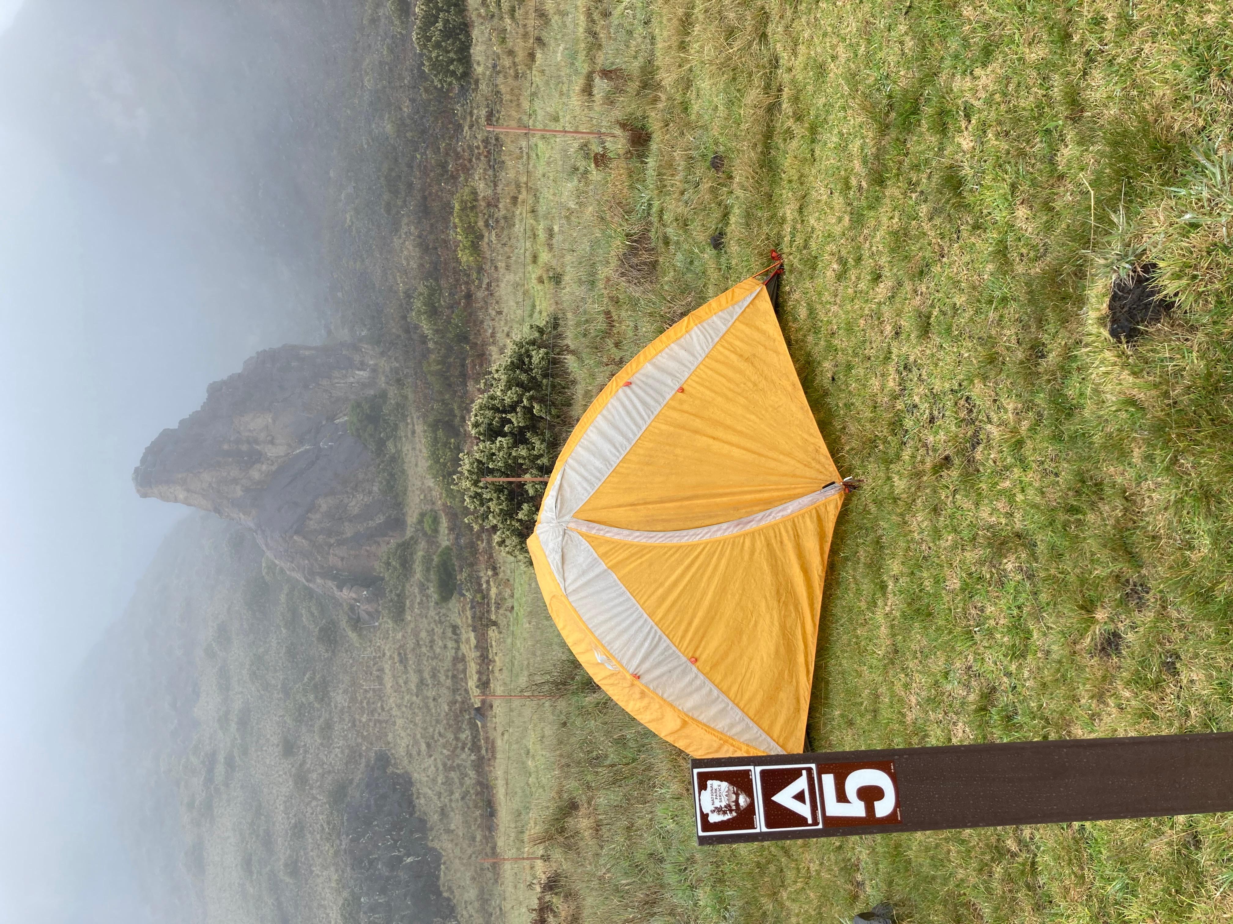 orange tent set up in grassy area with mist and clouds in background