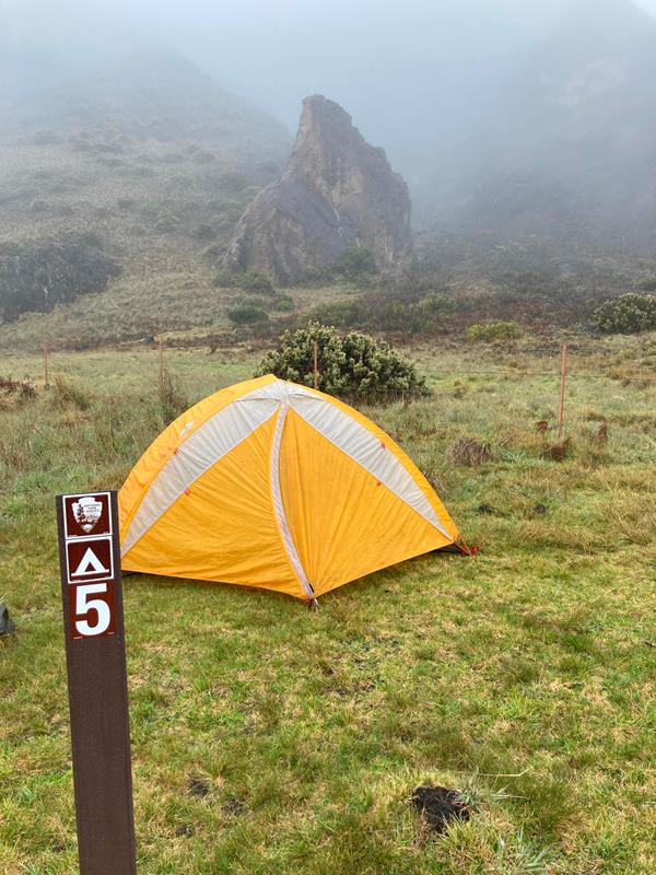 orange tent set up in grassy area with mist and clouds in background