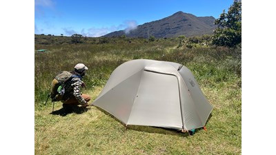 camper setting up tent in grassy area with mountain peak in background
