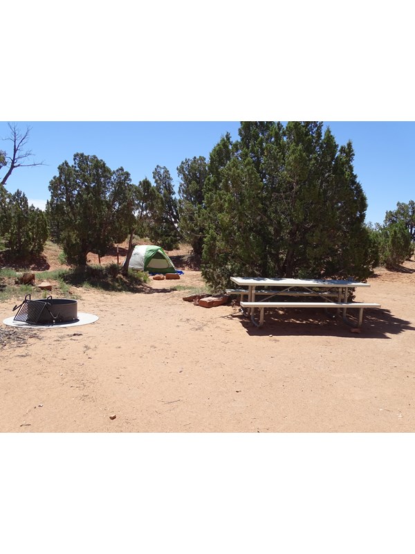 a tent is set up on a red dirt campsite with a fire pit and picnic table