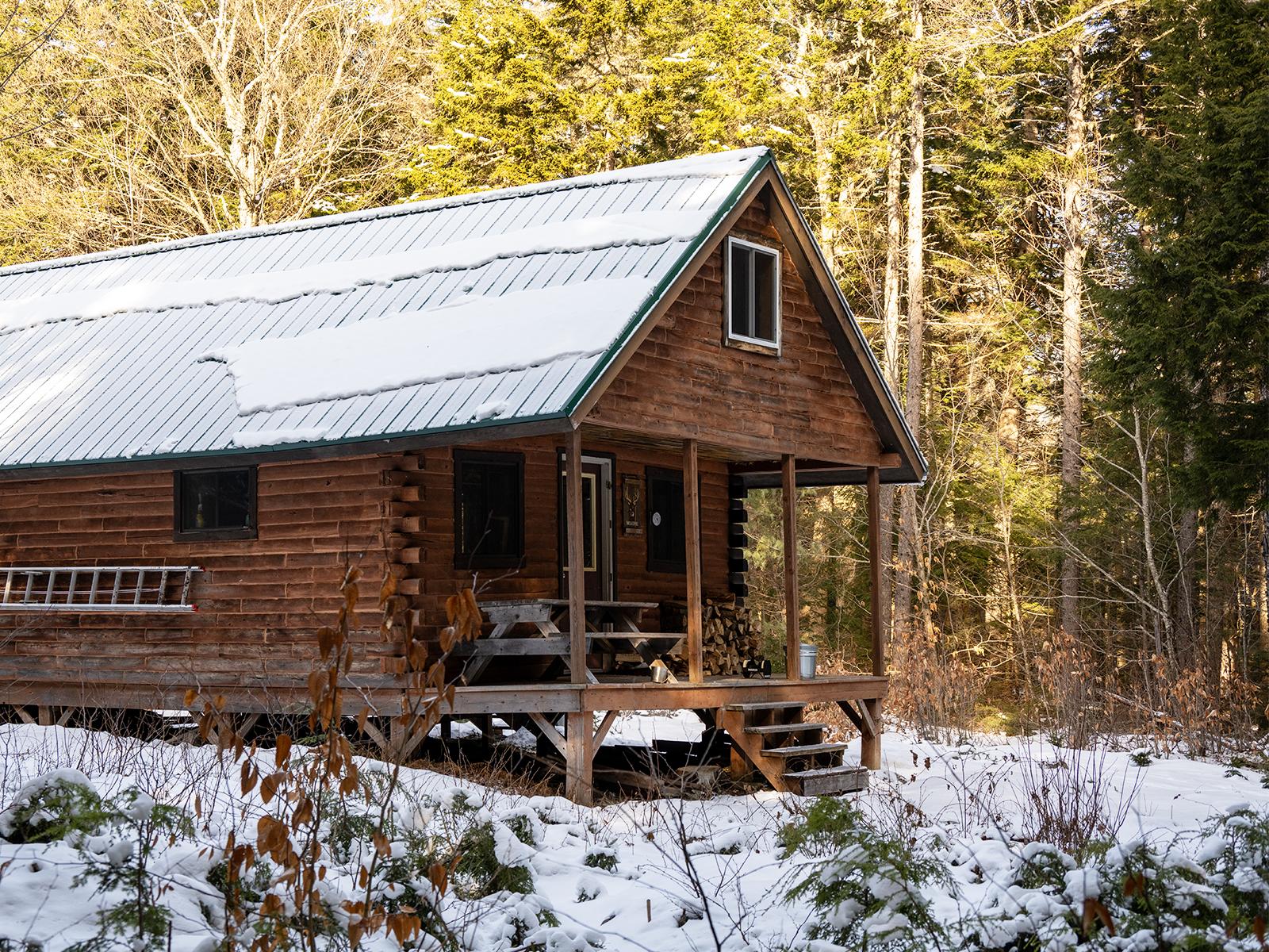 Side view of a log cabin in the woods with snow on the ground.