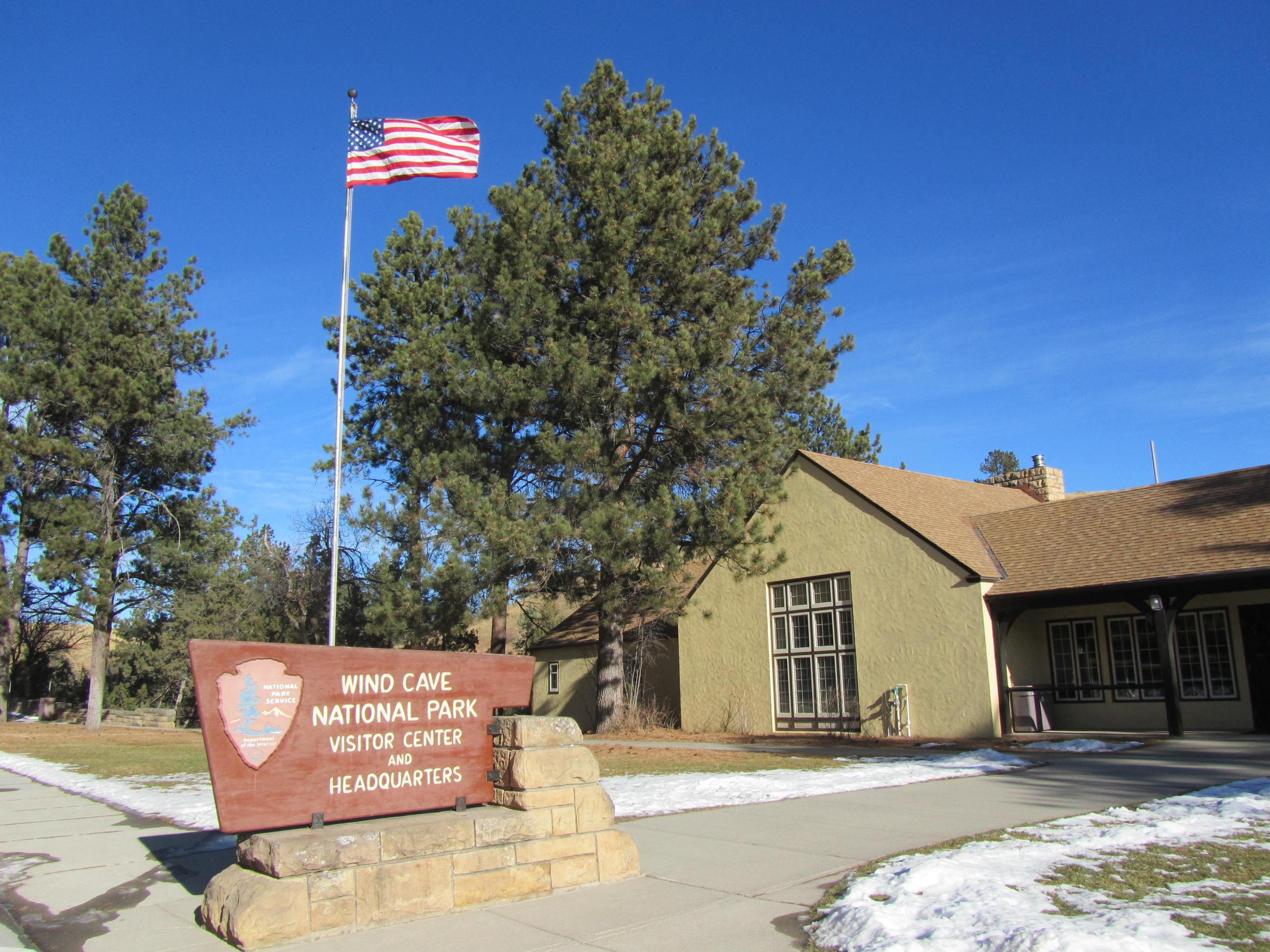 a yellow building with a brown roof and trim and a sign in front reading "wind cave national park"