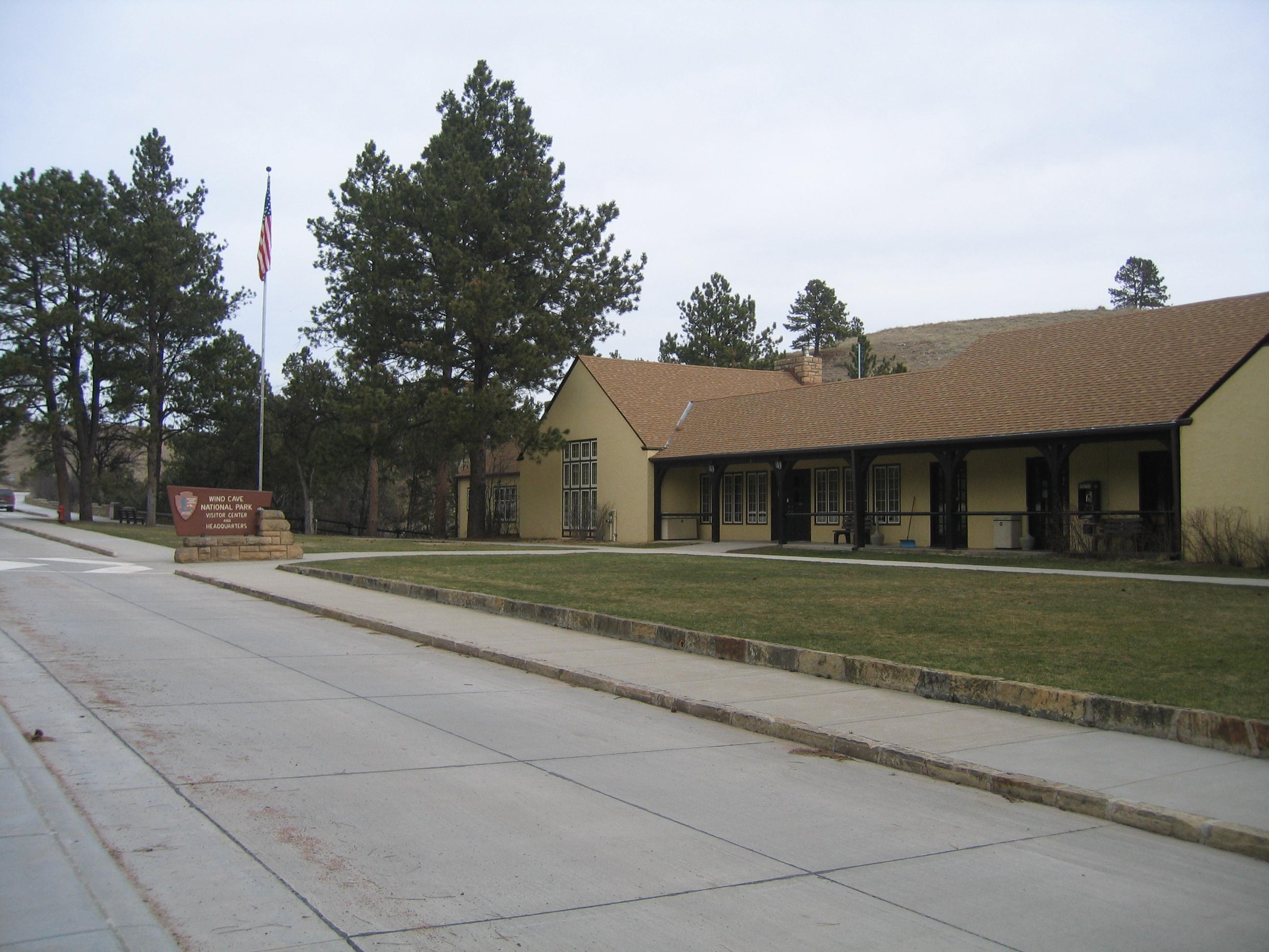 a yellow building with a brown roof and trim, with a wide green lawn and driveway
