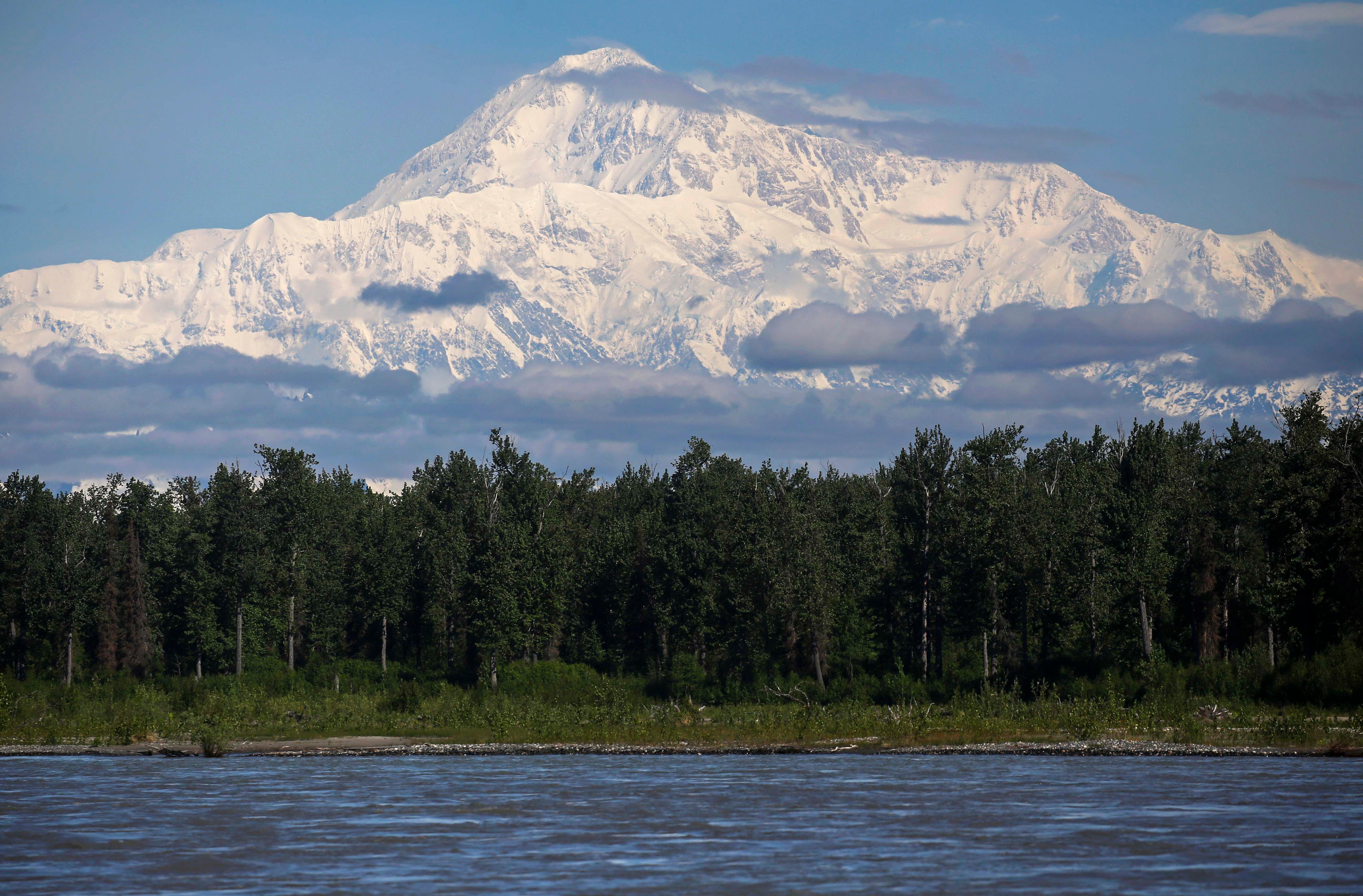 A huge snowy mountain looming over a landscape of forests and water