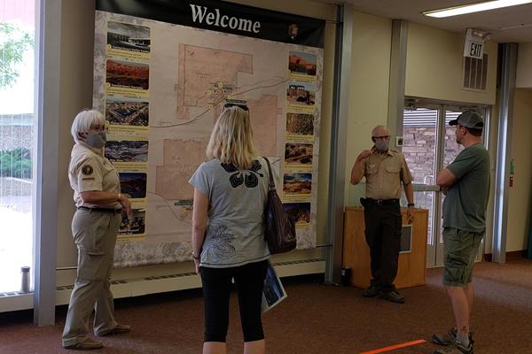 Two masked volunteers at the map talking to two visitors.