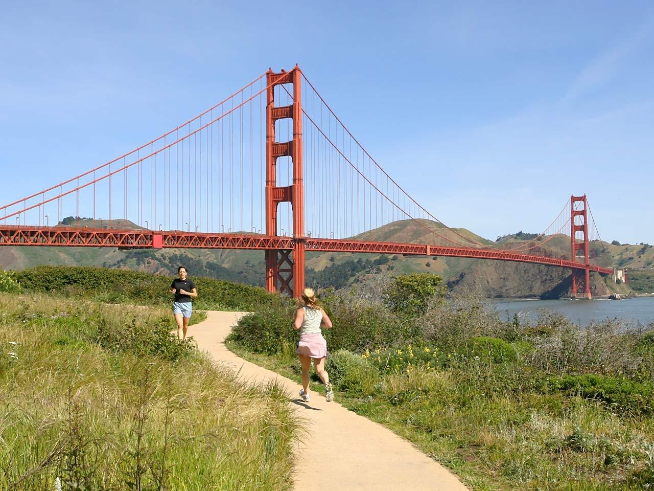 Person jogging along a path with golden gate bridge in the background.