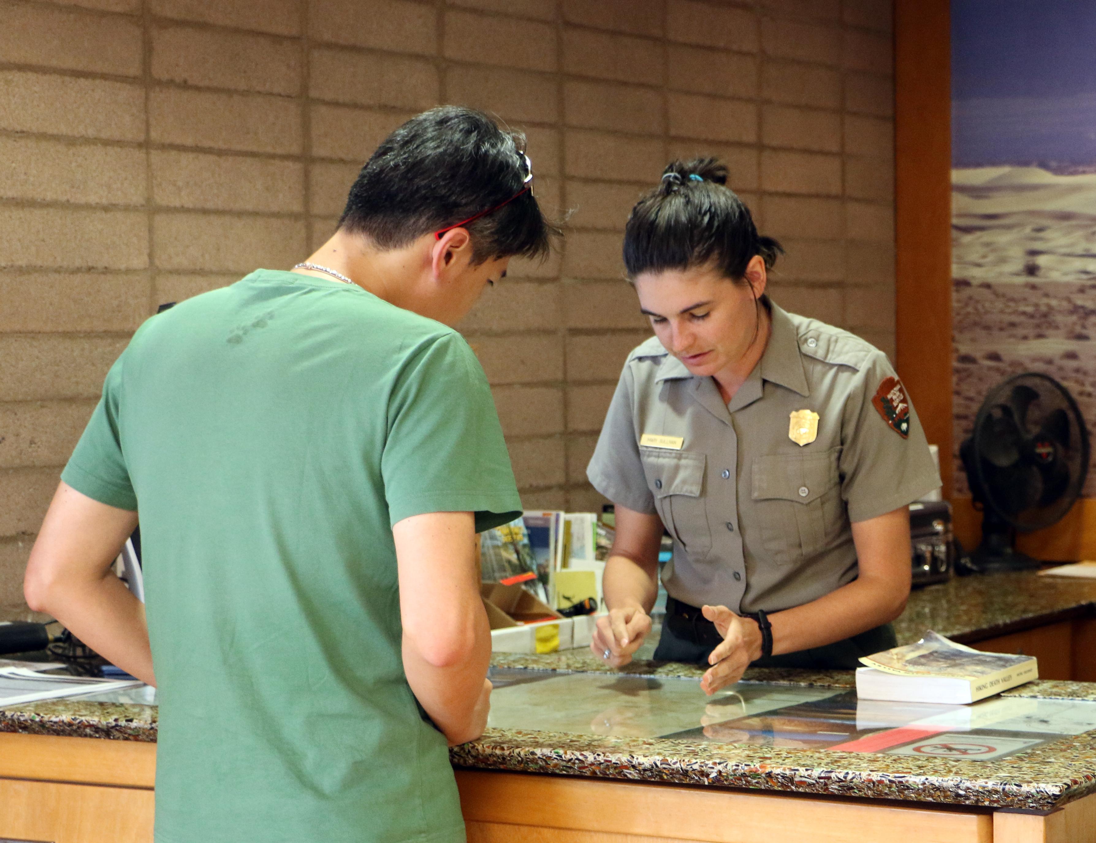 A ranger and a visitor look at a map displayed on a desk.