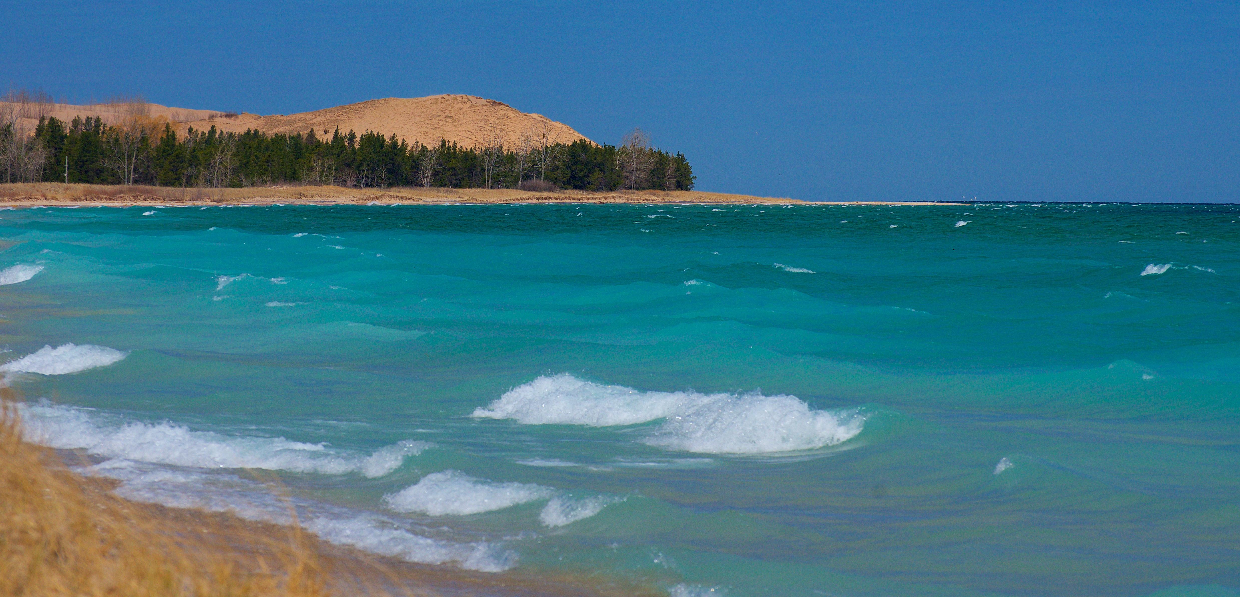 Waves crashing to shore with sand dunes in the background